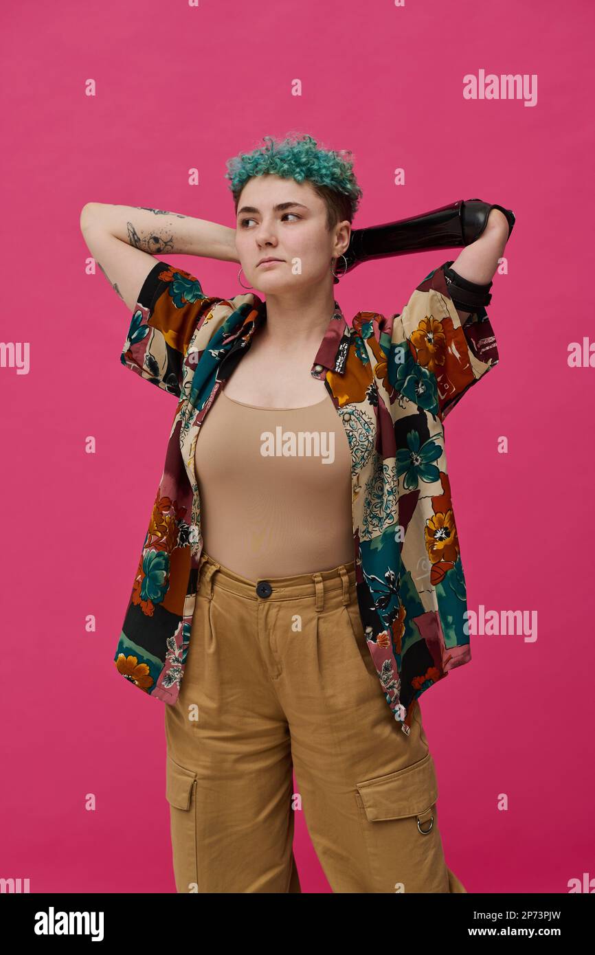 Portrait of young woman with prosthetic arm in stylish clothing posing against pink background Stock Photo