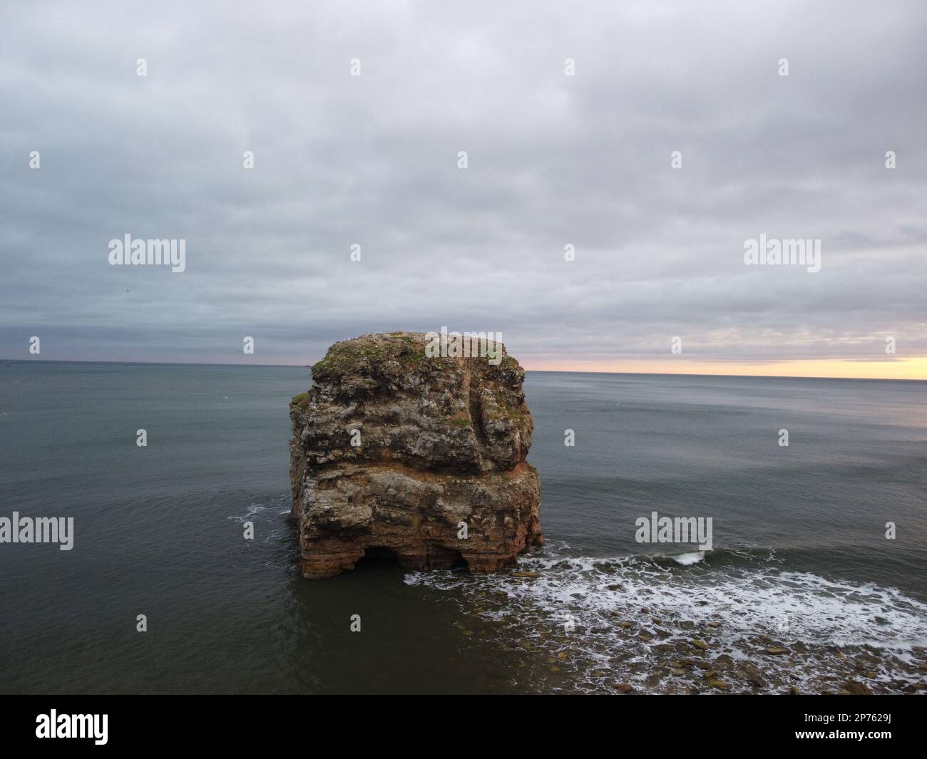 A rugged, craggy rock formation jutting out of the ocean at sunset ...