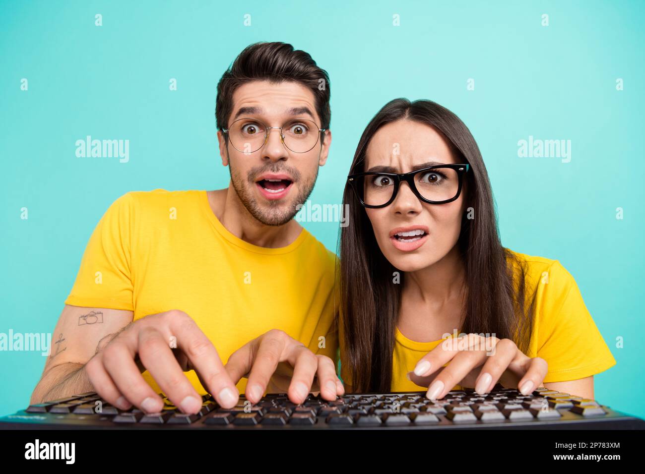 Closeup portrait of young geeks it specialists wear yellow t-shirt writing keyboard browsing esport betting isolated on aquamarine color background Stock Photo