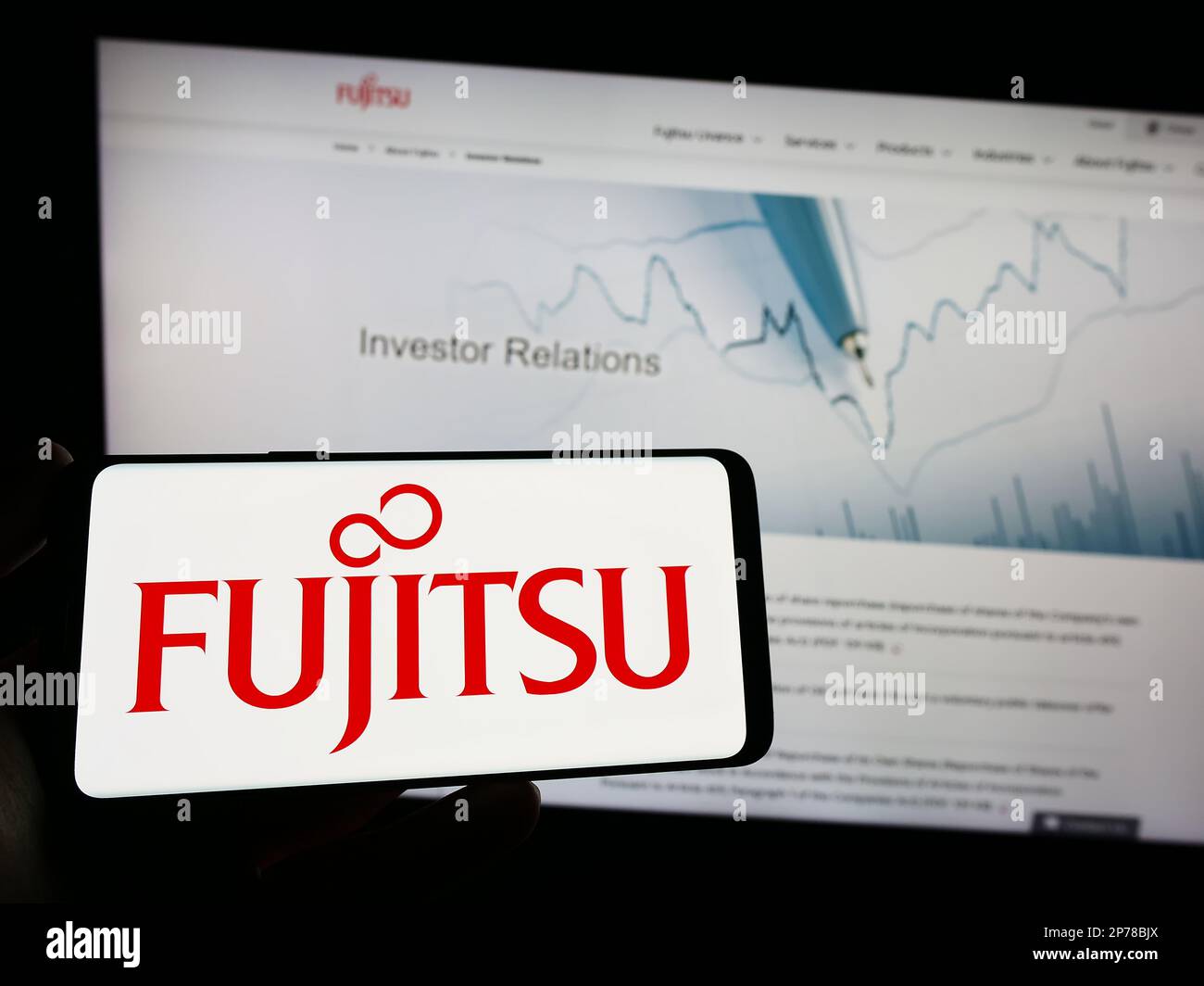 Person holding mobile phone with logo of Japanese ICT company Fujitsu Limited on screen in front of business web page. Focus on phone display. Stock Photo