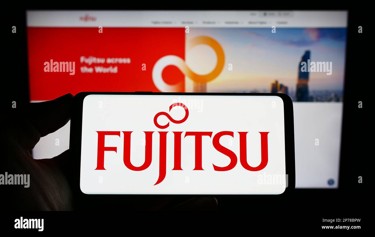 Person holding smartphone with logo of Japanese ICT company Fujitsu Limited on screen in front of website. Focus on phone display. Stock Photo
