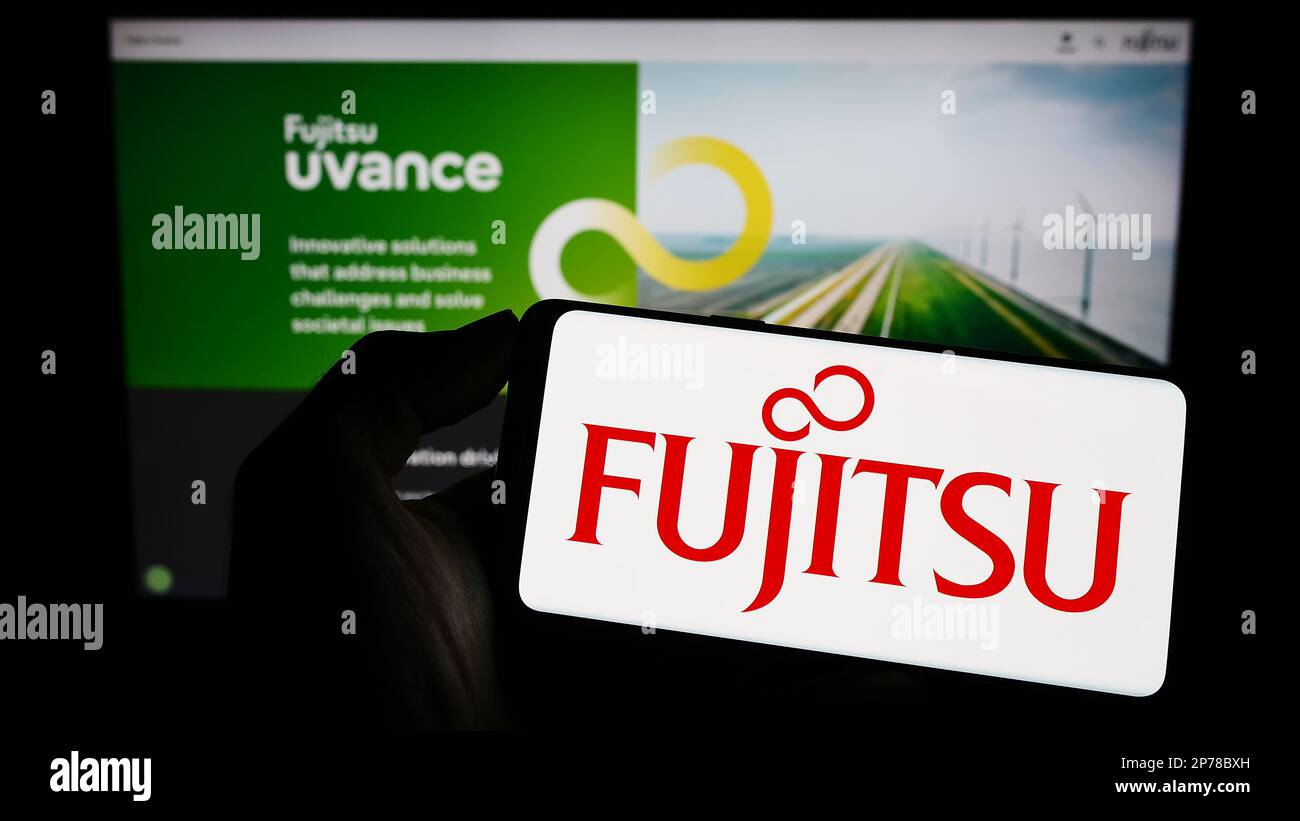 Person holding cellphone with logo of Japanese ICT company Fujitsu Limited on screen in front of business webpage. Focus on phone display. Stock Photo