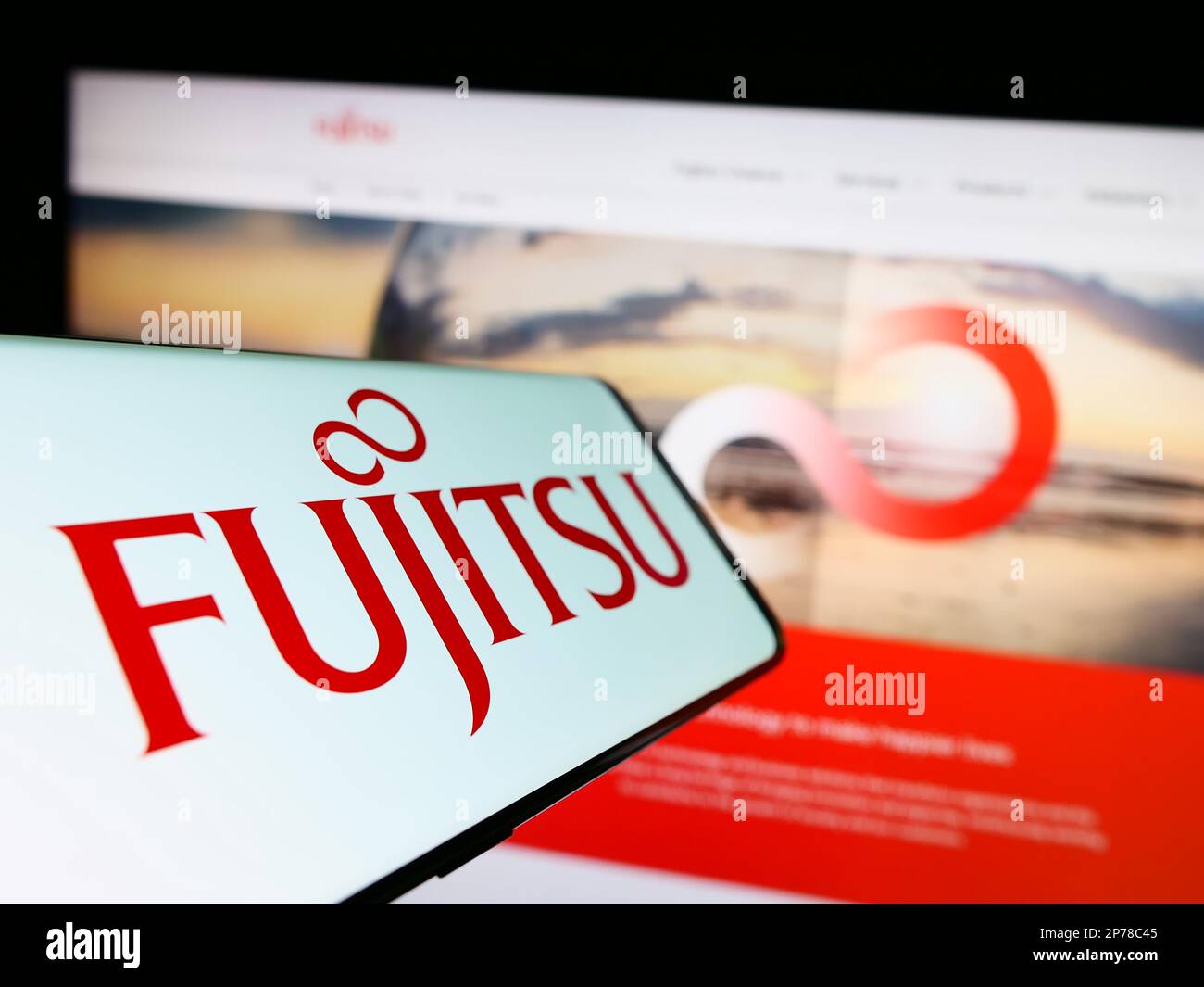 Mobile phone with logo of Japanese ICT company Fujitsu Limited on screen in front of business website. Focus on center-left of phone display. Stock Photo