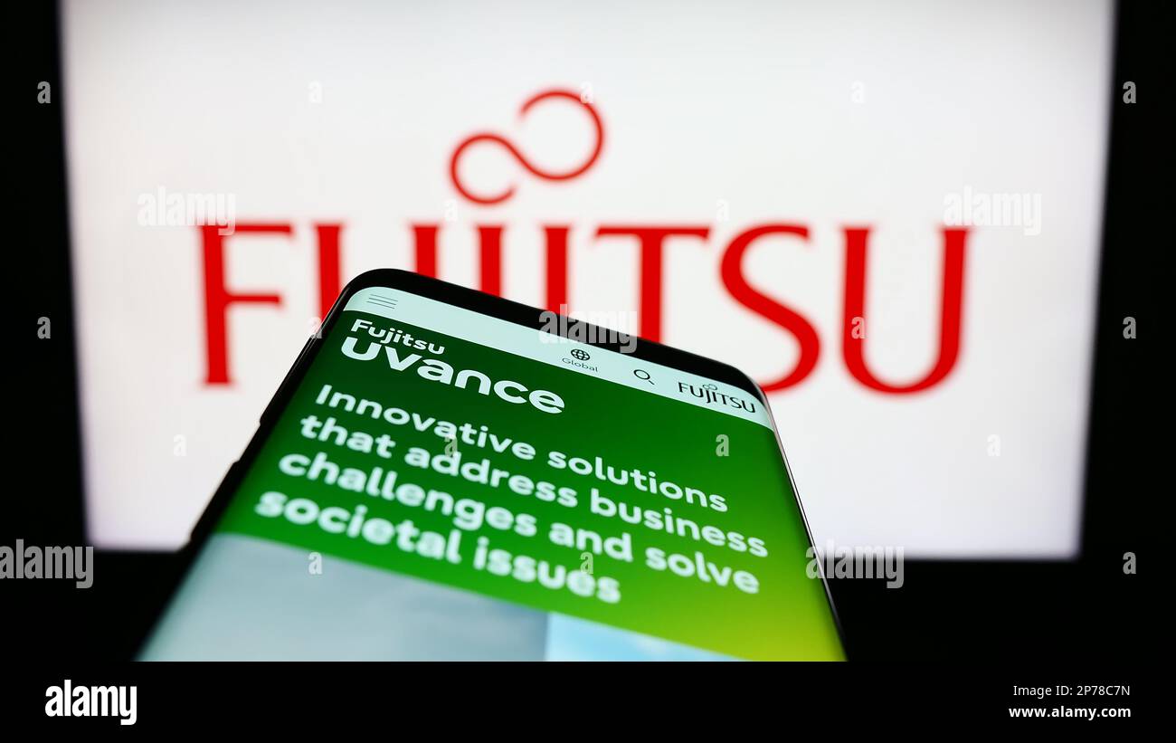 Smartphone with website of Japanese ICT company Fujitsu Limited on screen in front of business logo. Focus on top-left of phone display. Stock Photo