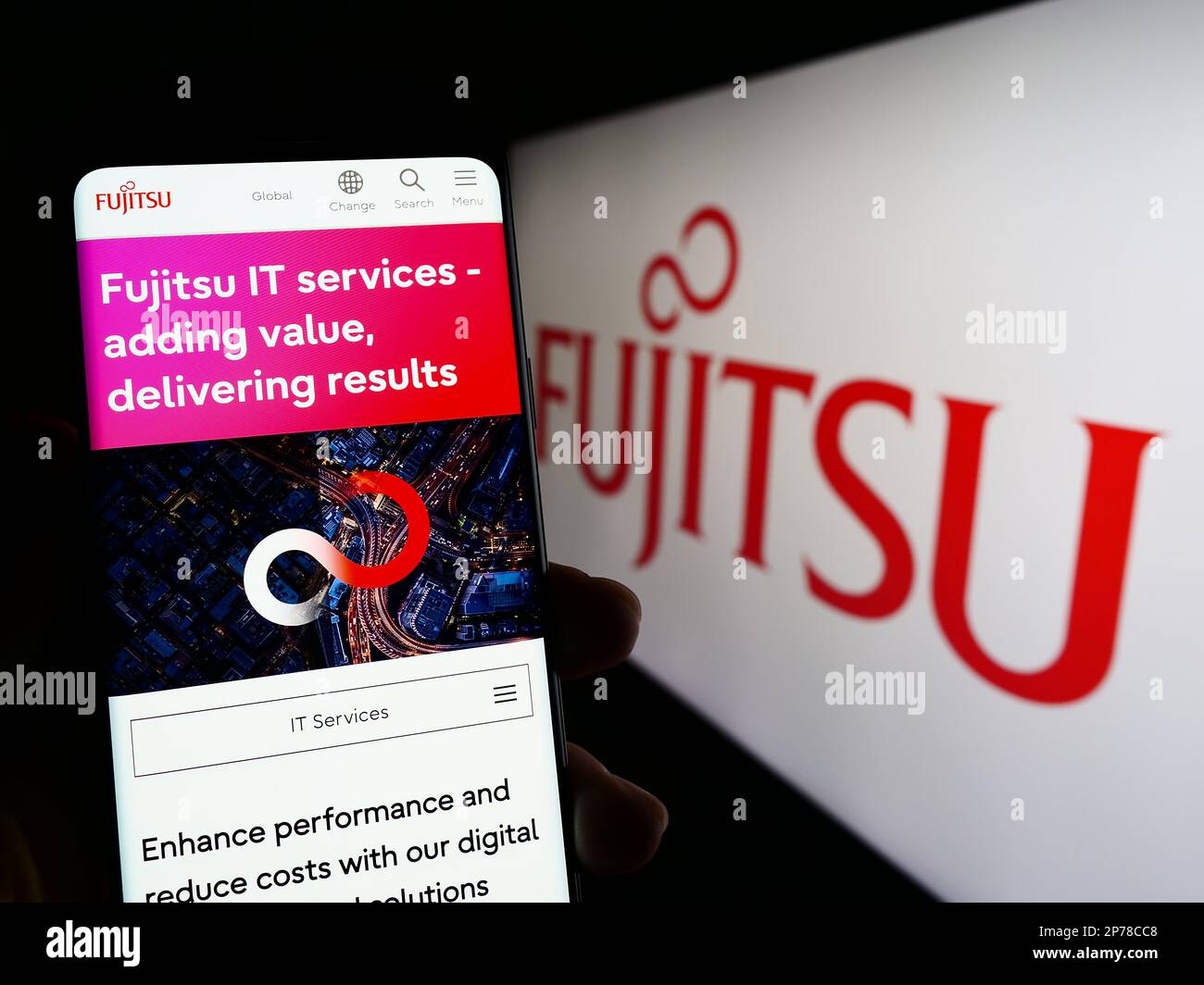 Person holding cellphone with webpage of Japanese ICT company Fujitsu Limited on screen in front of logo. Focus on center of phone display. Stock Photo