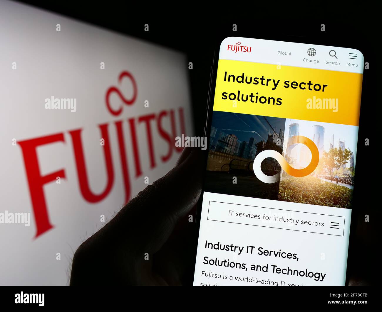 Person holding smartphone with web page of Japanese ICT company Fujitsu Limited on screen in front of logo. Focus on center of phone display. Stock Photo