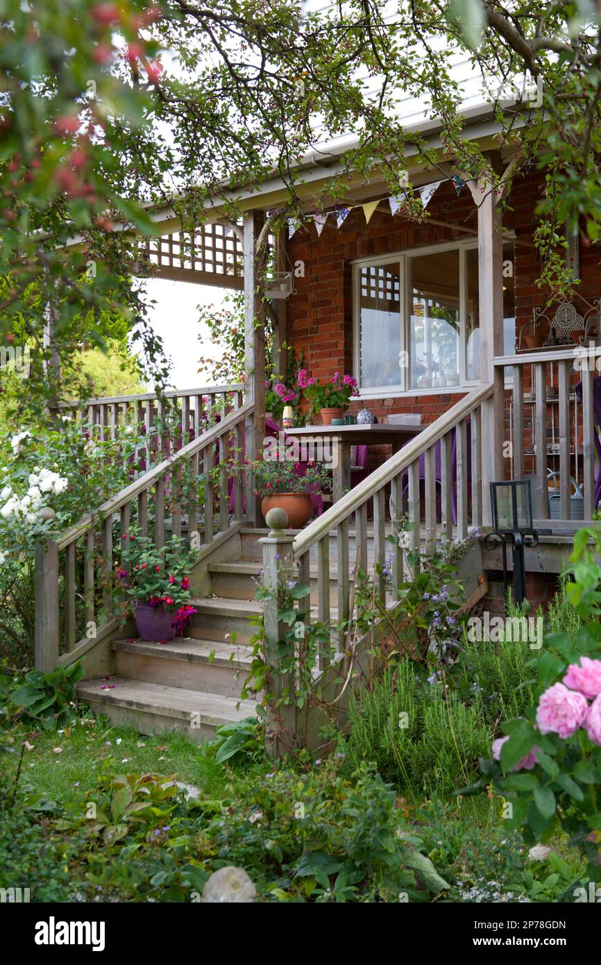 Raised wooden decking area with steps and outdoor seating, surrounded by climbing roses Stock Photo