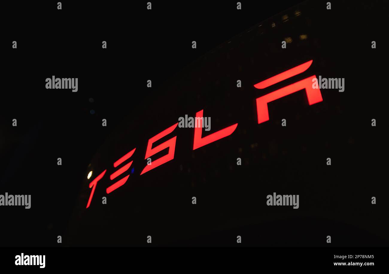 Glowing bright red Tesla logo on a dark night background close-up Stock