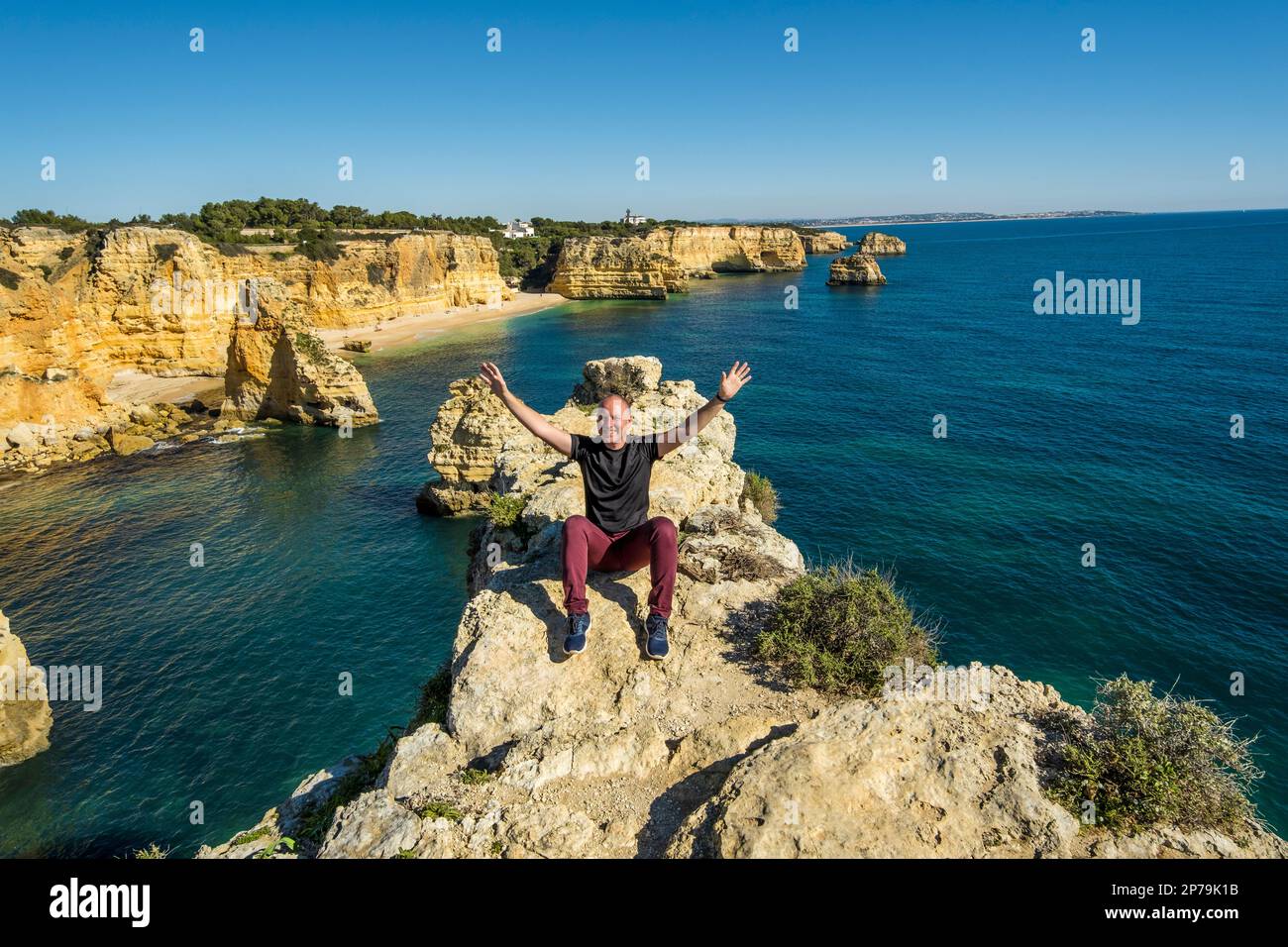 Happy man sitting with hands up on the top of cliffs at Marinha beach, Algarve, Portugal Stock Photo