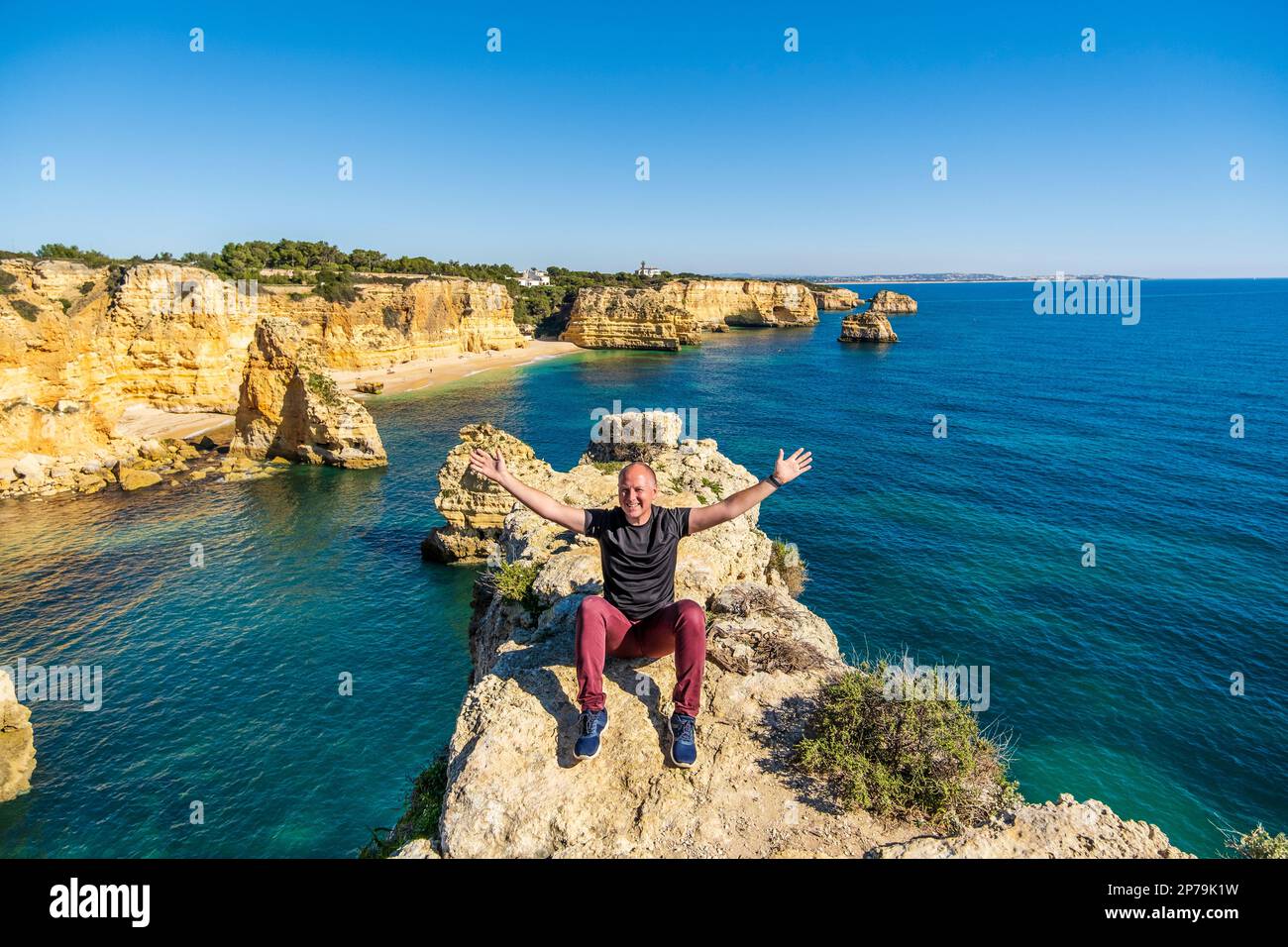 Happy man sitting with hands up on the top of cliffs at Marinha beach, Algarve, Portugal Stock Photo