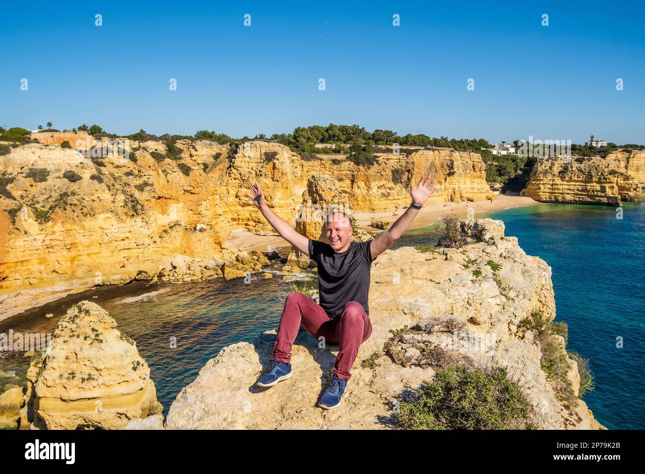 Happy man sitting with hands up on the top of cliffs at Marinha beach, Algarve, Portugal Stock Photo