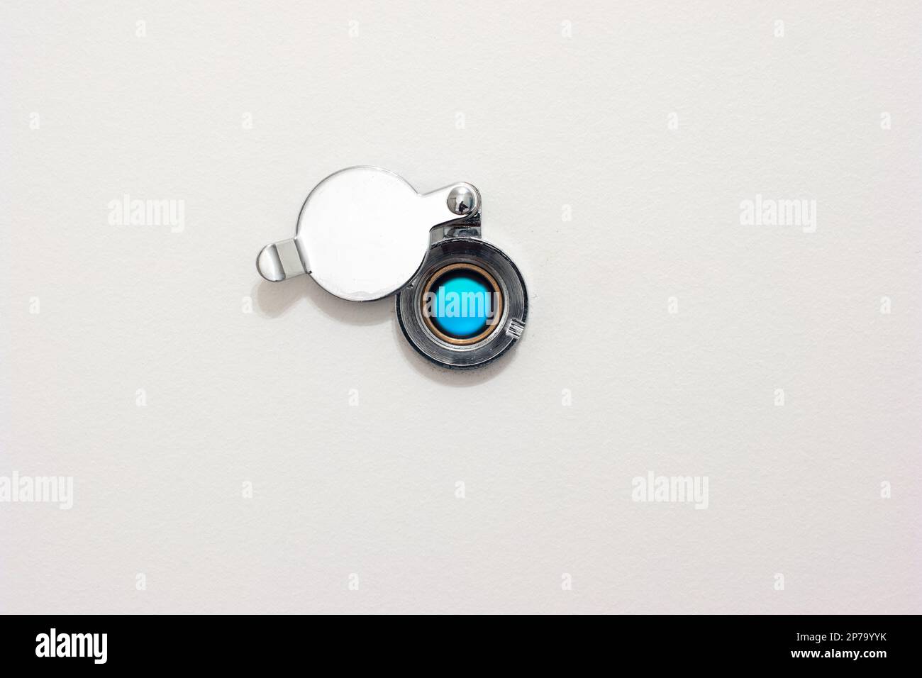 Home door peephole with metal lid cover white wood background macro close up shot. Stock Photo