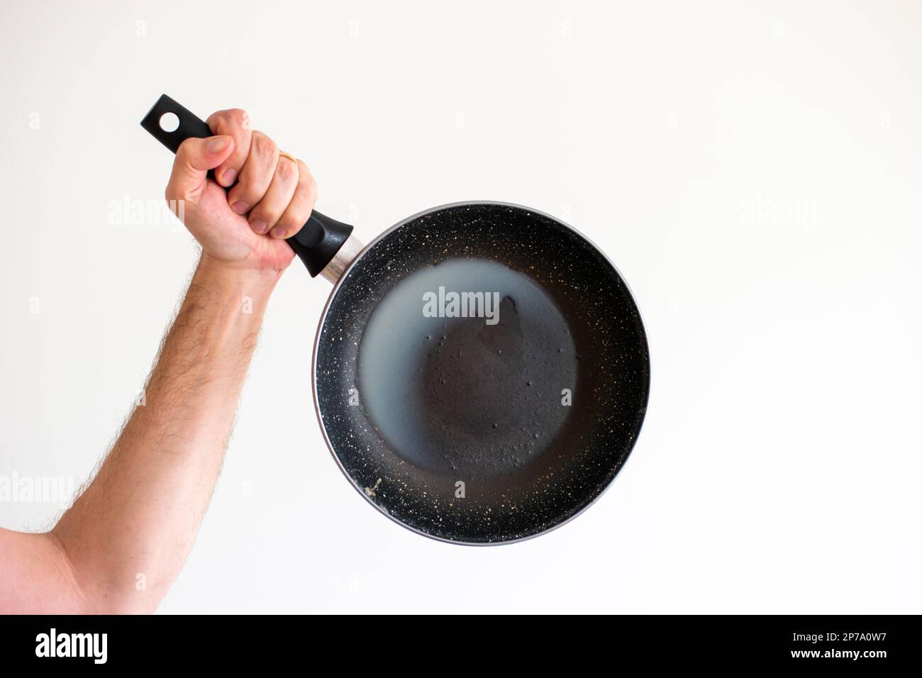 Caucasian male hand holding an old frying pan stained with hardened