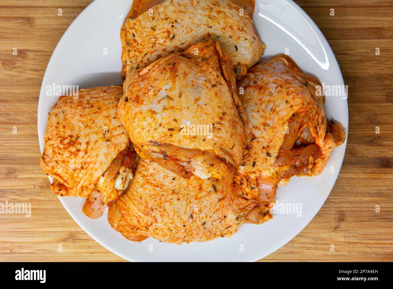 Raw chicken thighs with condiments on a white porcelain plate close up ...
