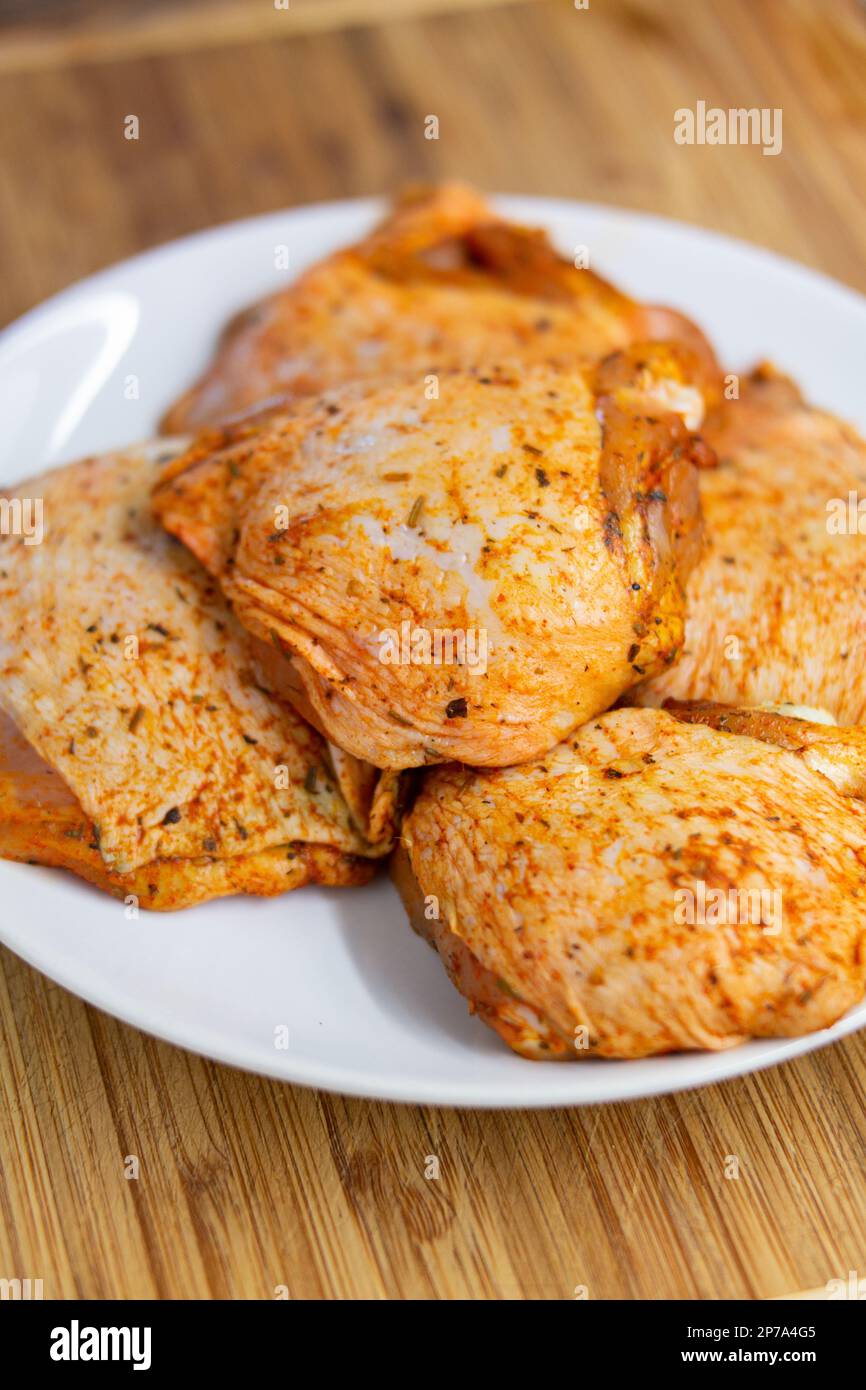 Raw chicken thighs with condiments on a white porcelain plate close up ...