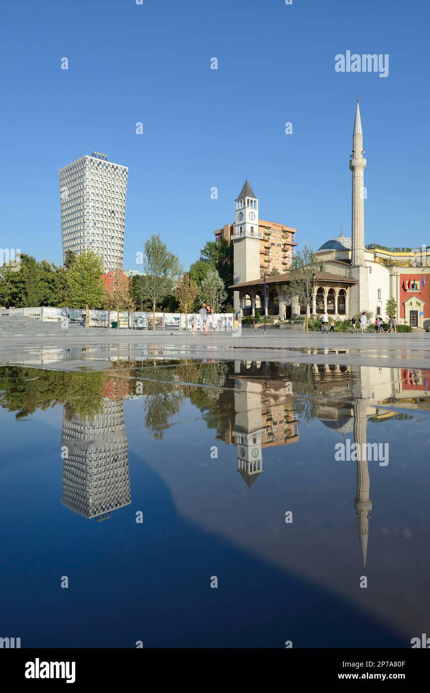 Plaza Hotel, Bell Tower and Ethem Bey Mosque reflected in a puddle, Skanderbeg Square, Tirana, Albania Stock Photo