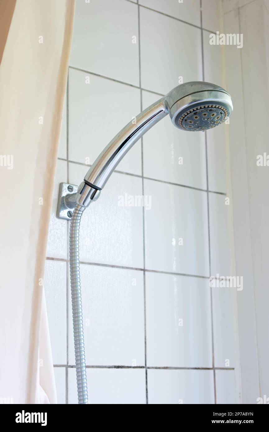 Shower head and cord hanging on the bathroom tile wall next to shower