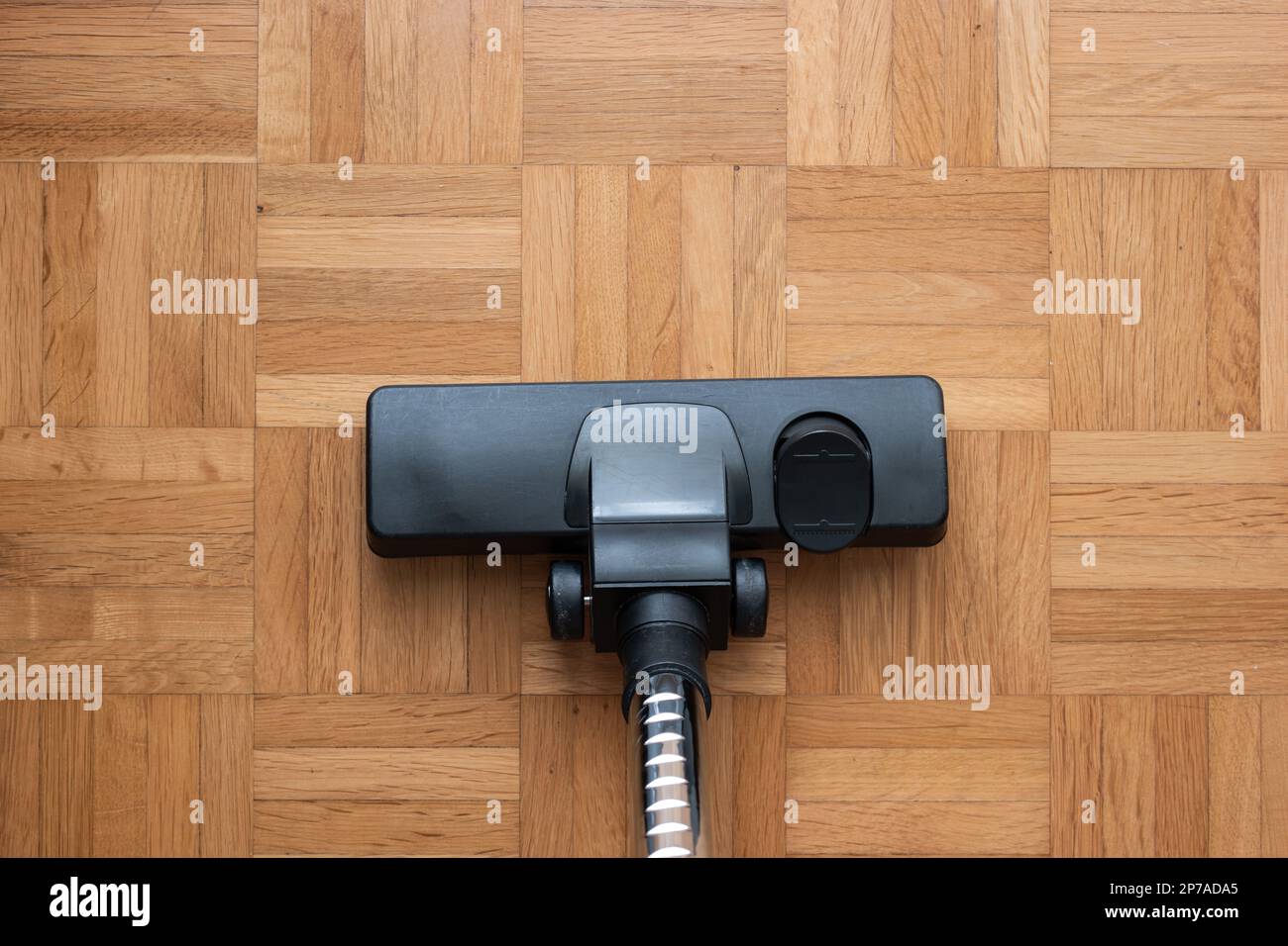Vacuum cleaner attachment on wooden floor tiles inside room, no people