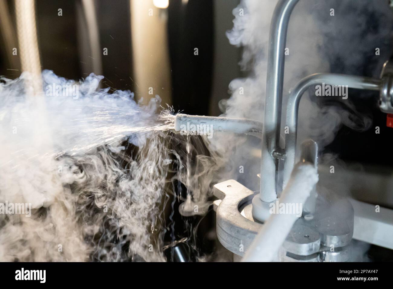 Liquid nitrogen splashing out along gas emanating from pressurized tank thermal rubber hose connected to metal pipes and red hand valves. Stock Photo