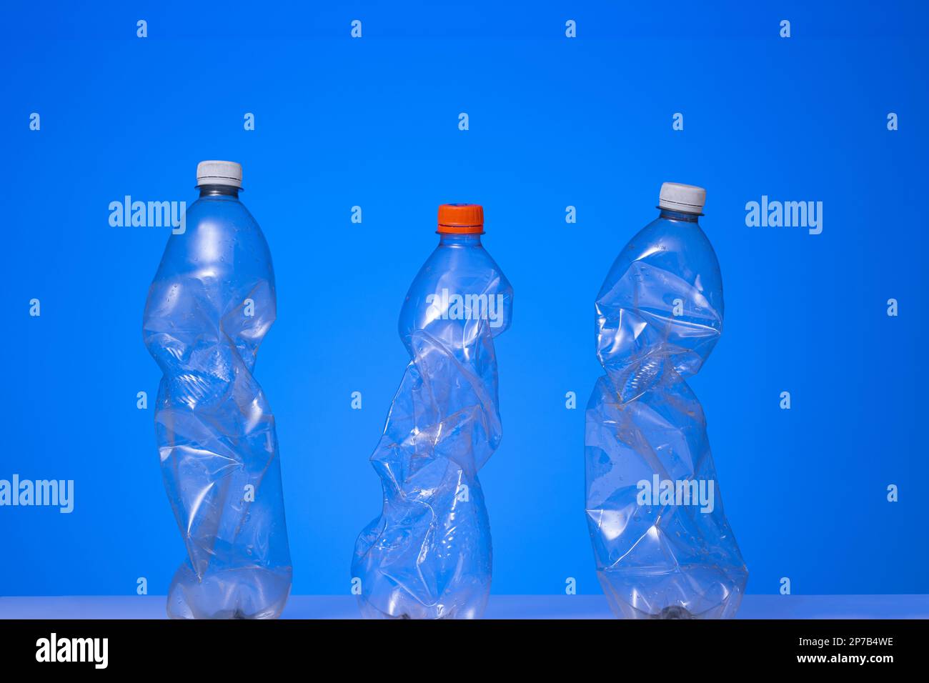 3 large clear squeezed plastic water bottles with close caps. Studio shot, isolated on blue, no people. Stock Photo