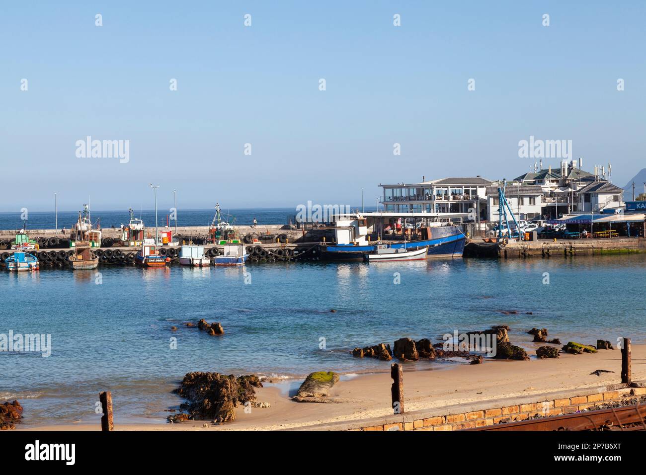 Fishing boats moored in Kalk Bay Harbour, Cape Town, Western Cape, South Africa at sunset, overlooked by a popular restaurant Stock Photo