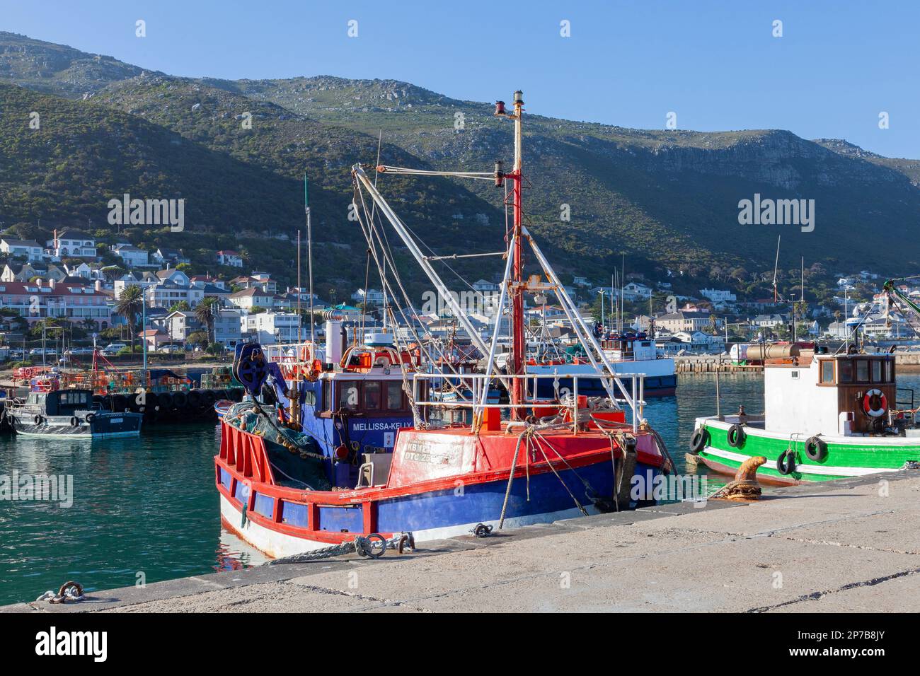 Fishing boats moored in Kalk Bay Harbour, Cape Town, Western Cape, South Africa at sunset with Kalk Bay visible behind Stock Photo