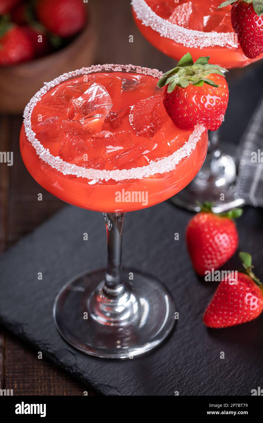 Strawberry margarita cocktail garnished with strawberries and salt rim on a black slate board Stock Photo