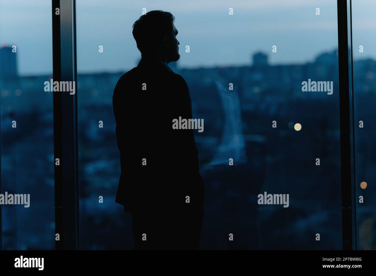 Silhouette of a Business Man looking out of high rise office window at night Stock Photo