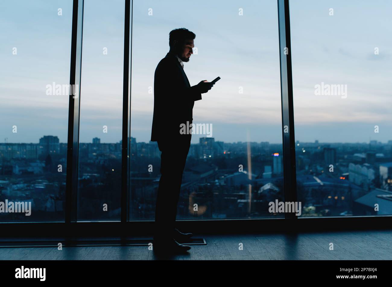 Silhouette of a Business Man looking out of high rise office window at night Stock Photo