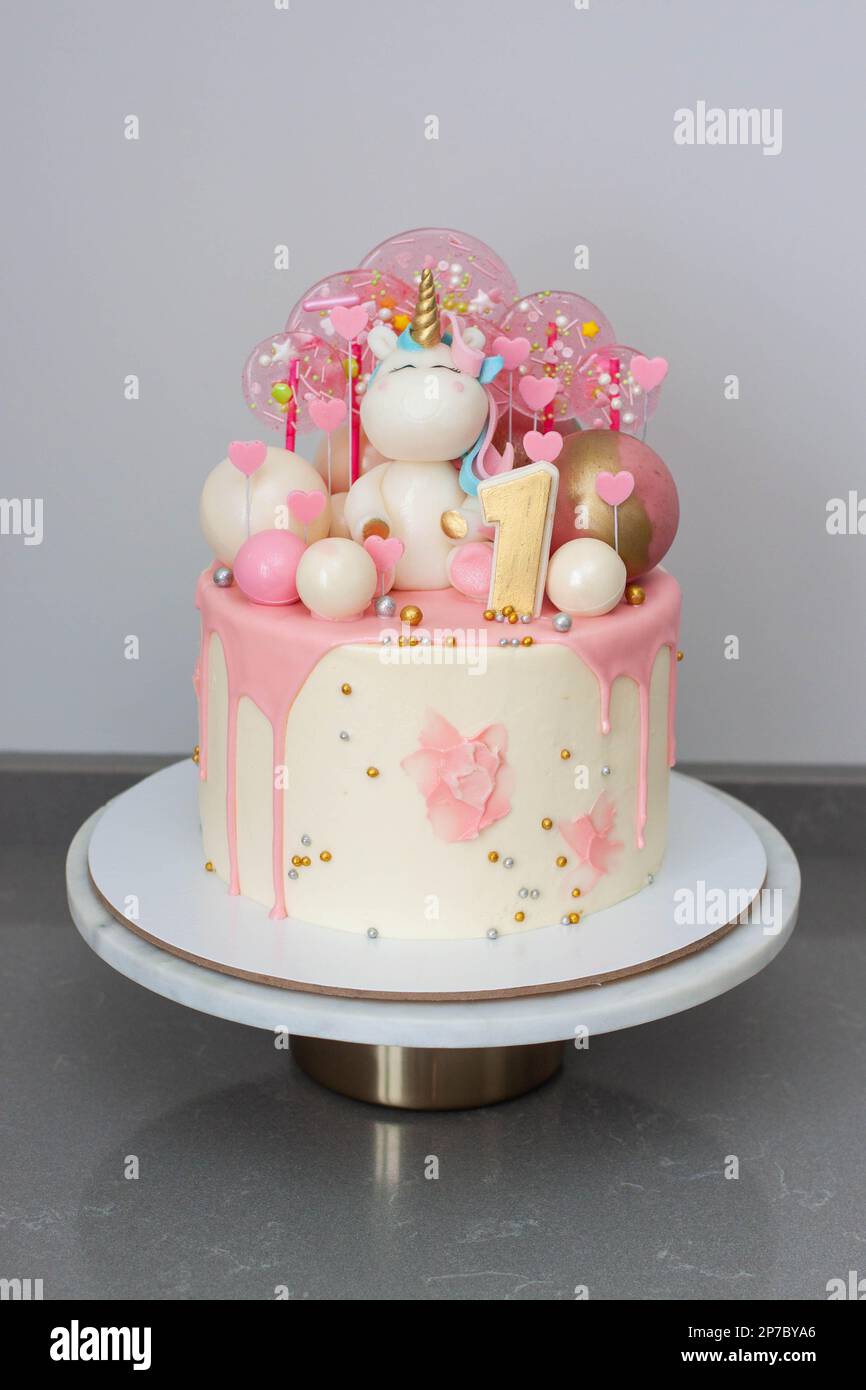 Cute birthday cake for a little girl with fondant unicorn, pink chocolate, lollipops, candies and hearts Stock Photo