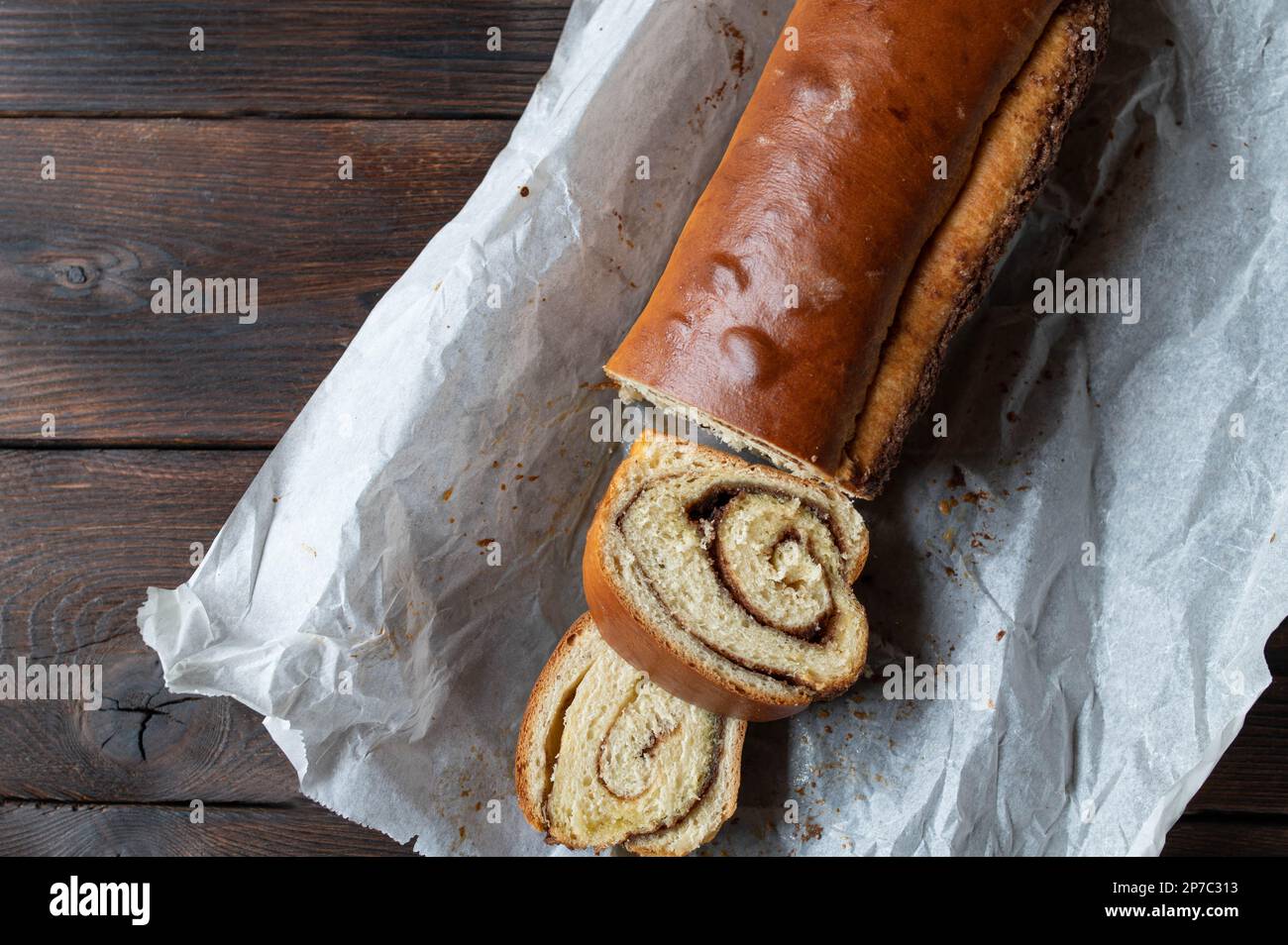 Loaf of yeast cake with cinnamon roll filling isolated on dark wooden table. Flat lay Stock Photo