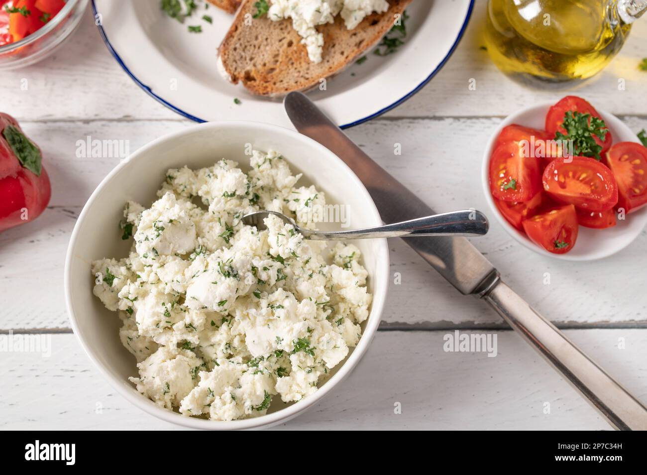 Marinated Feta cheese or sheep cheese with herbs and olive oil served for salad with roasted bread on white table Stock Photo