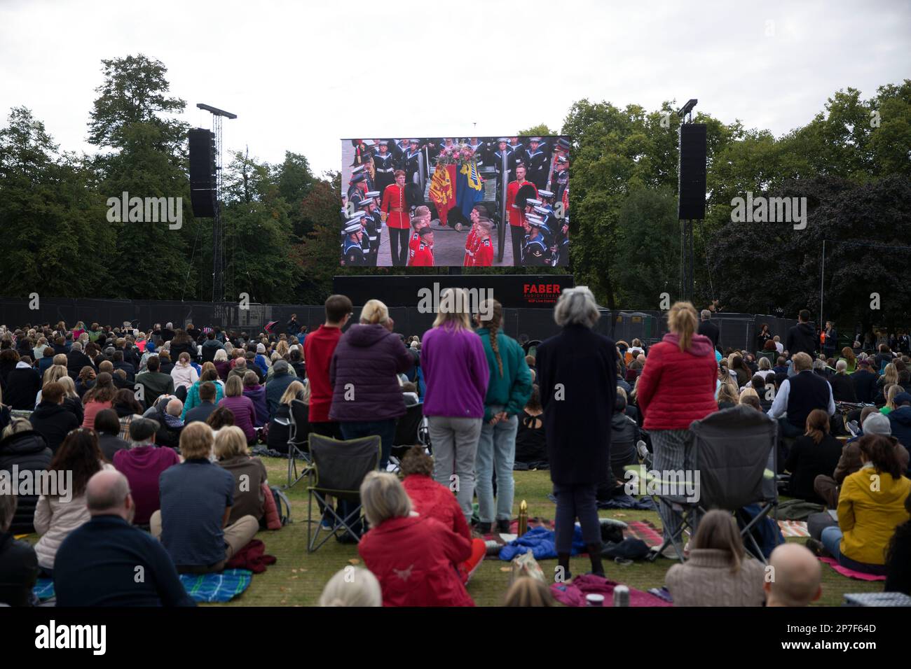 People watch the TV coverage of the late Queen Elizabeth II’s funeral day on a large screen in Hyde Park, London. Stock Photo