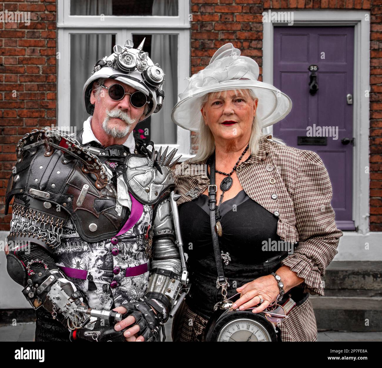 Portrait of a stylish retro futuristic middle aged steampunk couple standing outside a house. Stock Photo