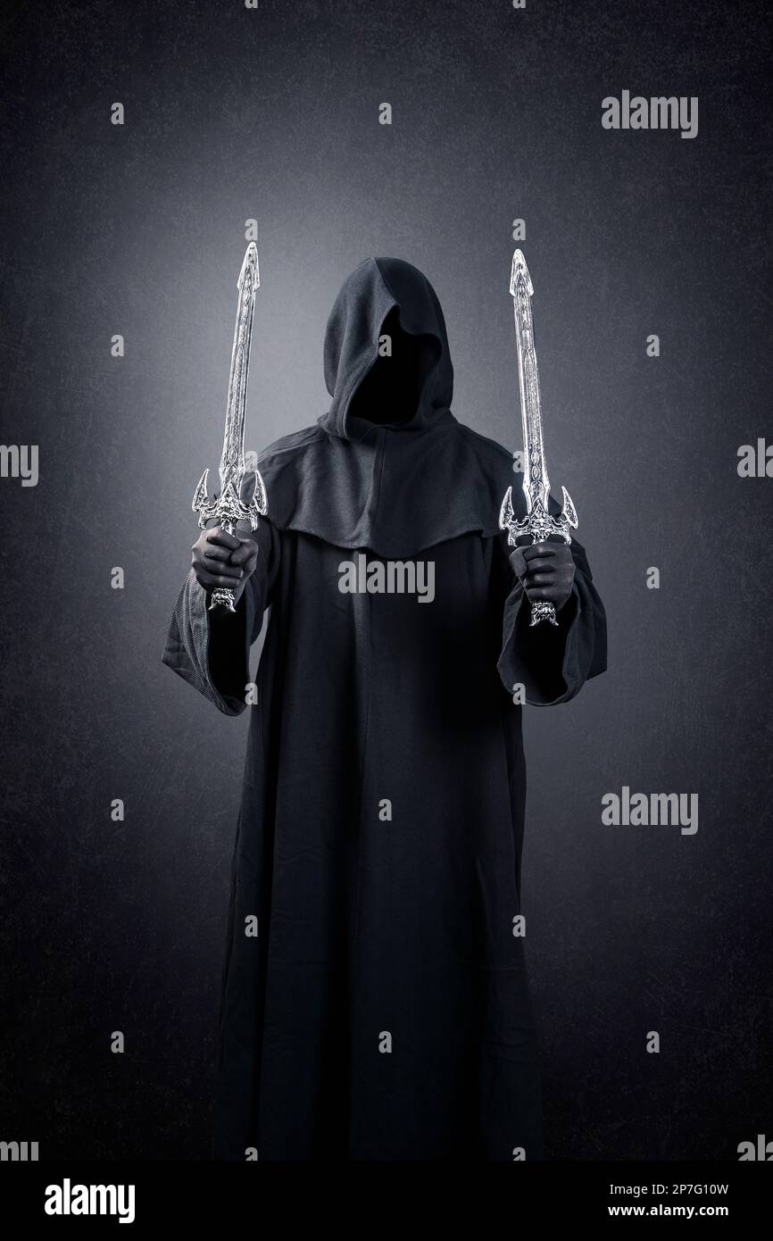 Dark knight with hooded cape and two swords over dark misty background Stock Photo