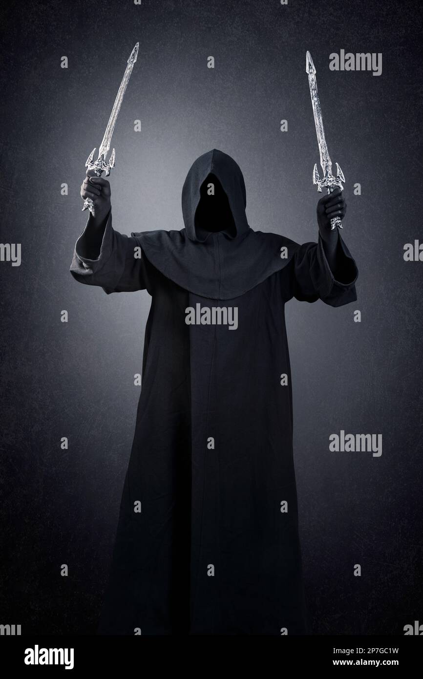 Dark knight with hooded cape and two swords over dark misty background Stock Photo