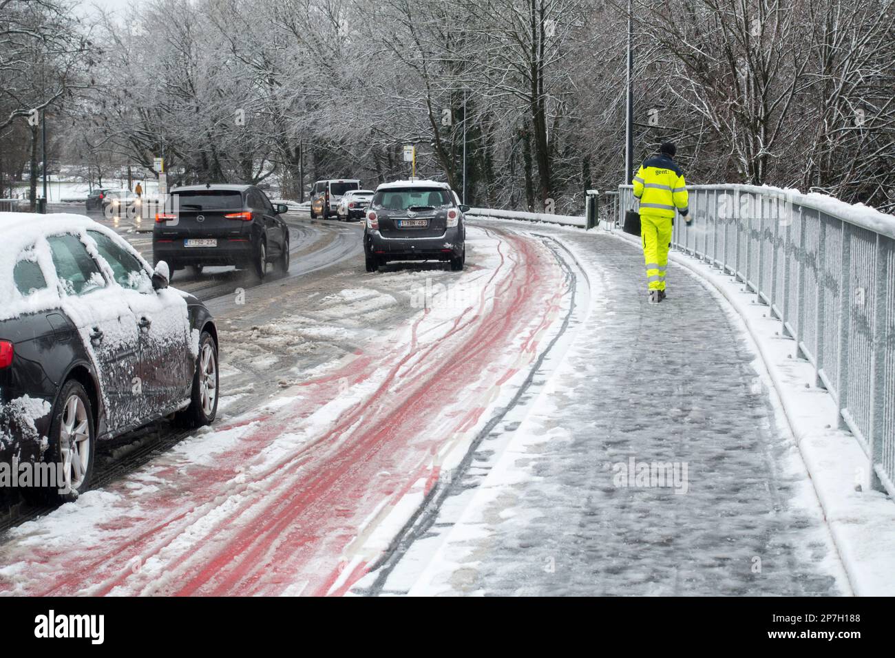 City worker spreading salt over slippery pavement on bridge covered in sleet during unexpected late snow shower in March 2023, Ghent, Belgium Stock Photo