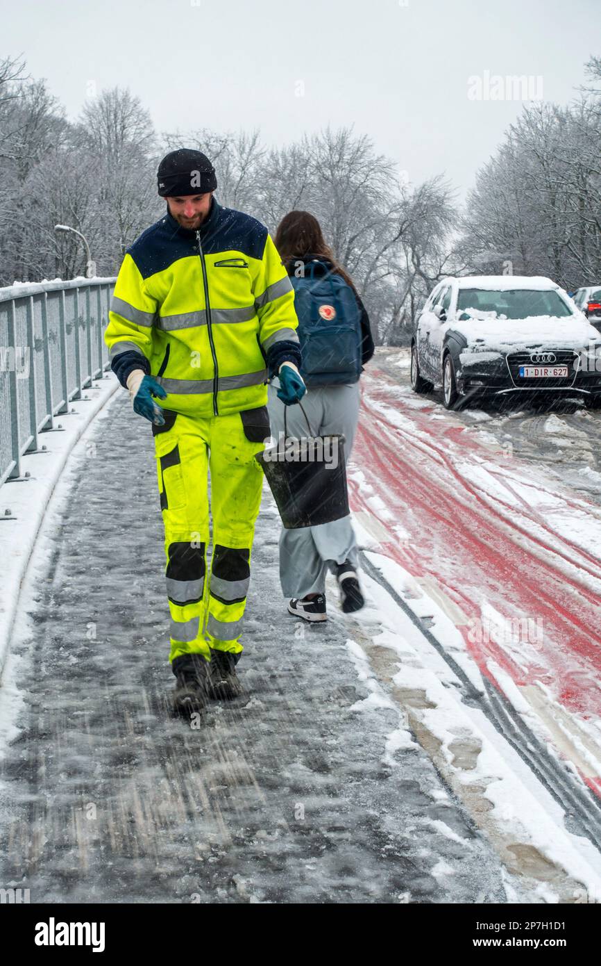 City worker spreading salt over slippery pavement on bridge covered in sleet during unexpected late snow shower in March 2023, Ghent, Belgium Stock Photo