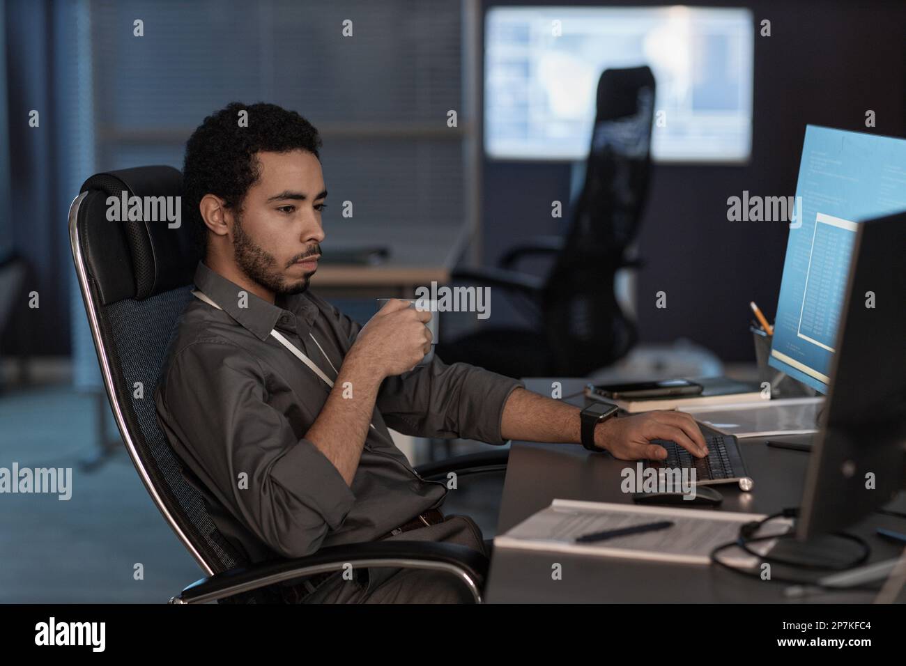 Side view portrait of man using computer and drinking coffee while working in data security office Stock Photo