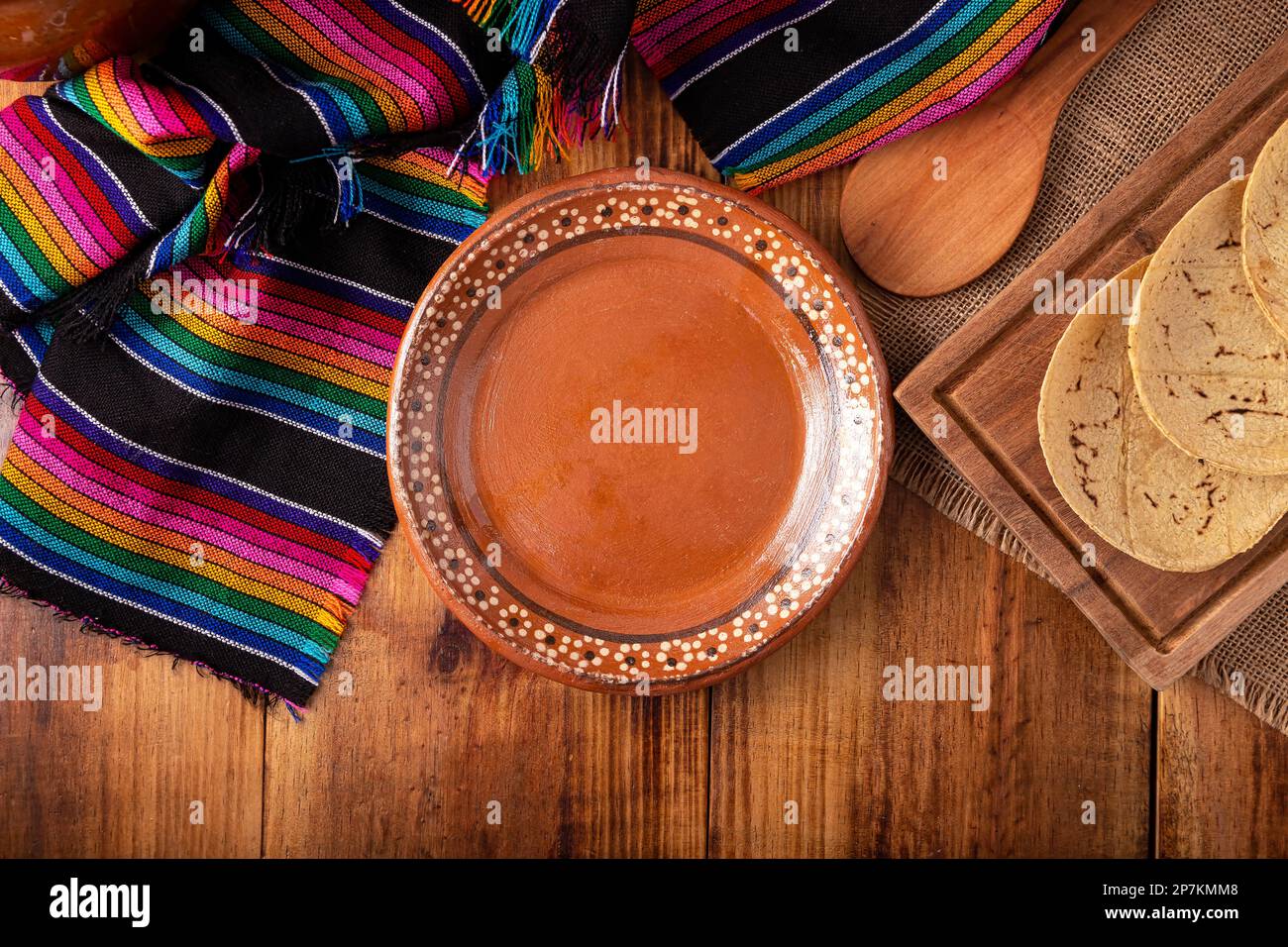 Cooking background with empty mud dish, mexican typical fabric on rustic wooden table. Table top view with copy space. Stock Photo