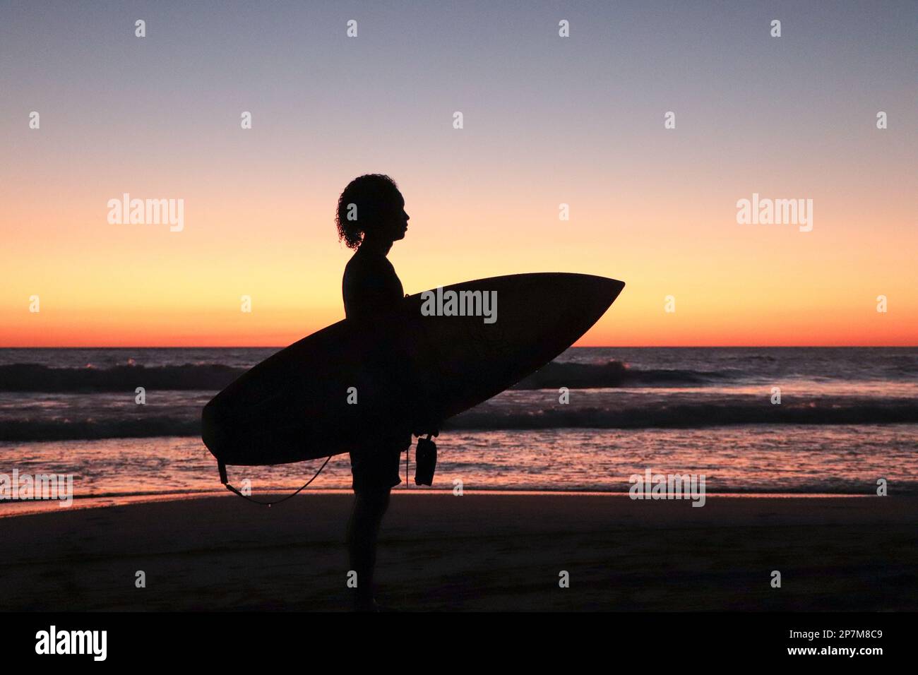 Silhouette of Oniel Lopez, young male surfer holding his surfboard at sunset on Jiquilillo beach, Nicaragua Stock Photo