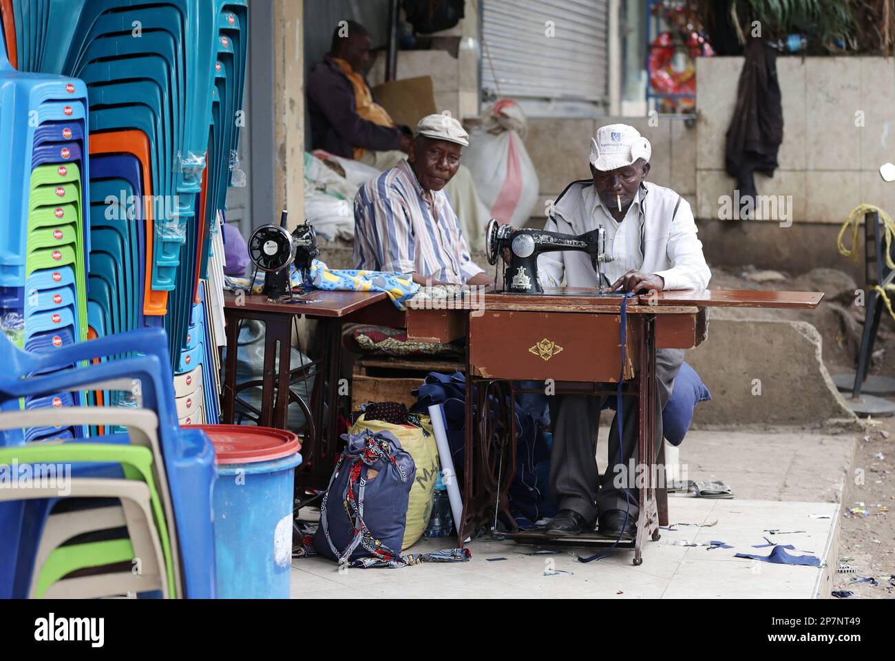 A tailor with a cigarette in his mouth sews on an Arusha street in Tanzania. Stock Photo
