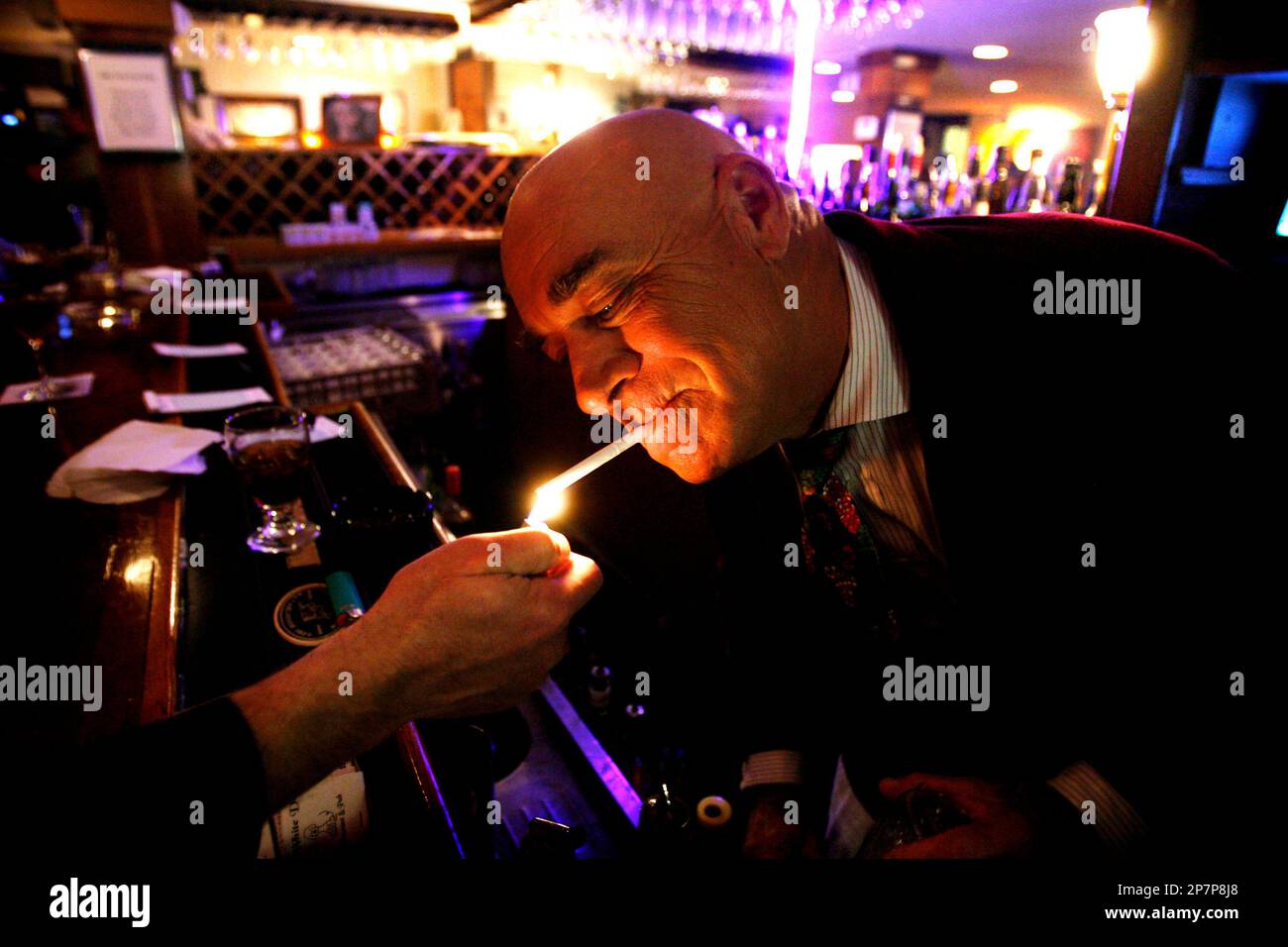 In this Nov. 30, 2009 photo, Barry Pruitt gets a light behind the bar at  his Fan restaurant, The White Dog, in Richmond, Va., during a "last gasp"  night of cigar and