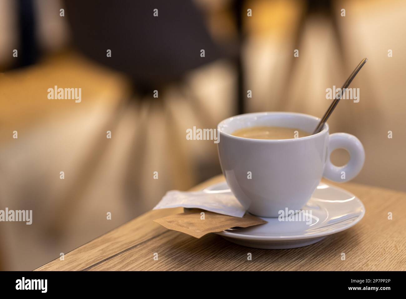 white cup of coffee on a saucer with sachets of sugar on a wooden table with blurry photo Stock Photo