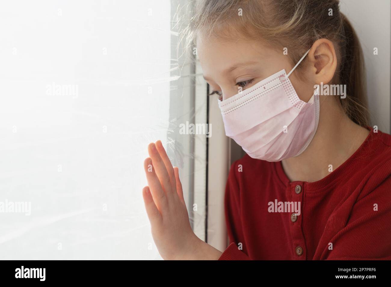 Sad child girl in a medical protective mask looks out the window Stock ...