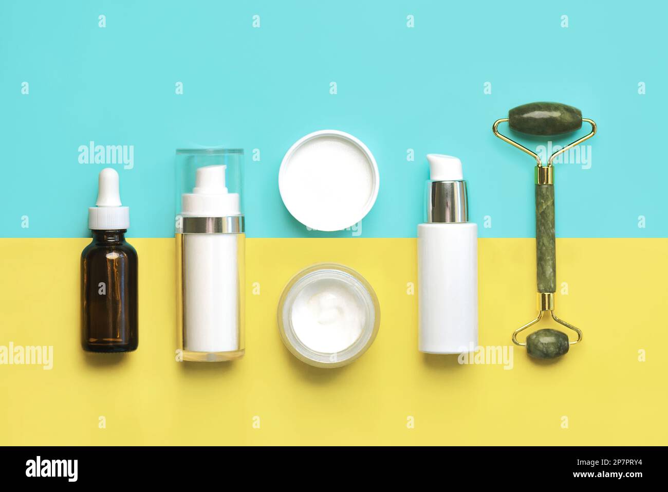 Set of cosmetics and jade massanger roller for skin care over blue and yellow background. Skin care products concept Stock Photo