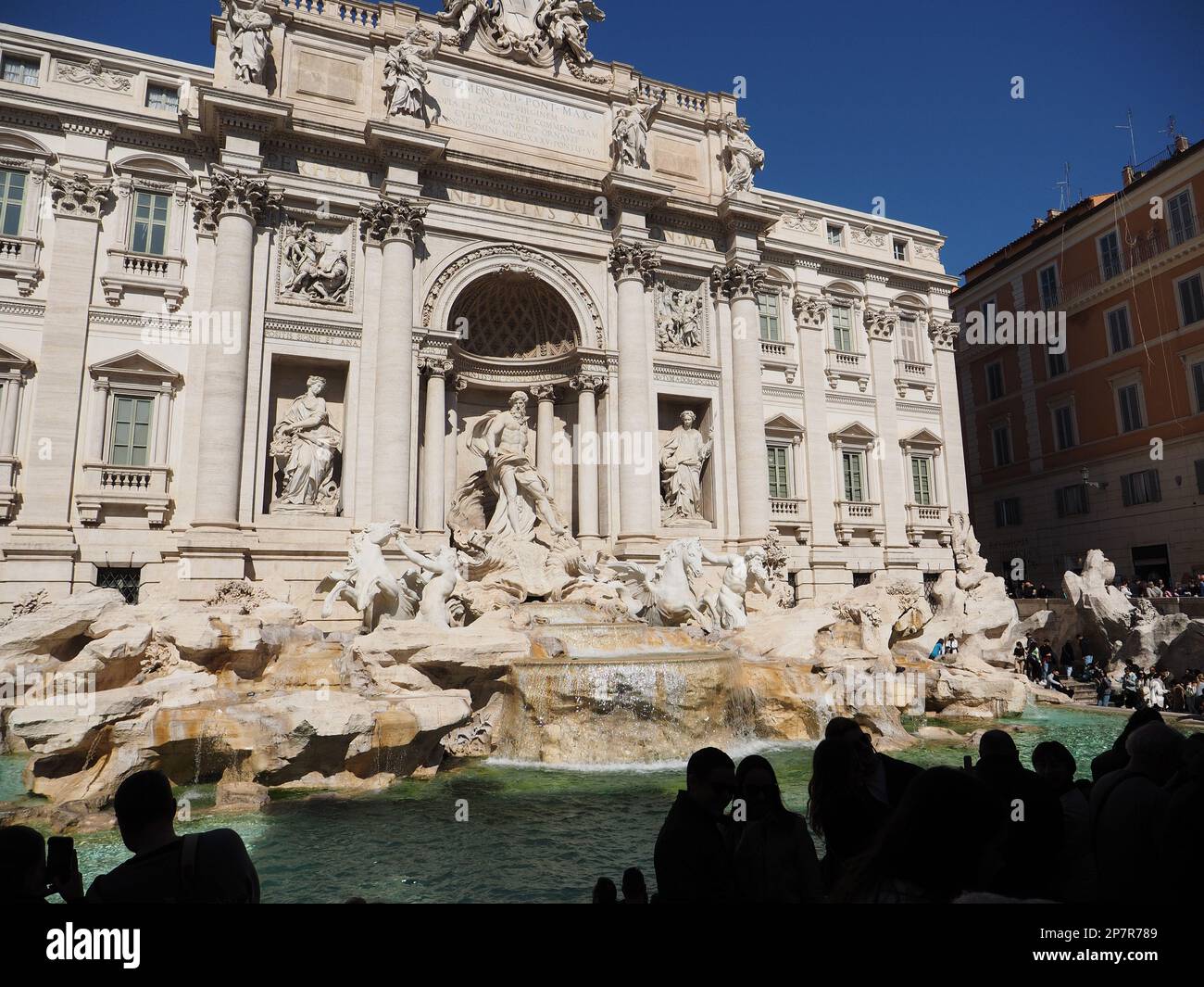 The famous Trevi fountain with silhouetted tourists in front and blue sky behind. A true icon, it is usually one of the most crowded places in the cit Stock Photo