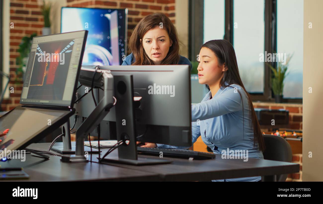 Diverse team of employees analyzing project component on multi screens, using engineering software on pc. Creative designers developing art on computer, discussing about 3D technology. Stock Photo