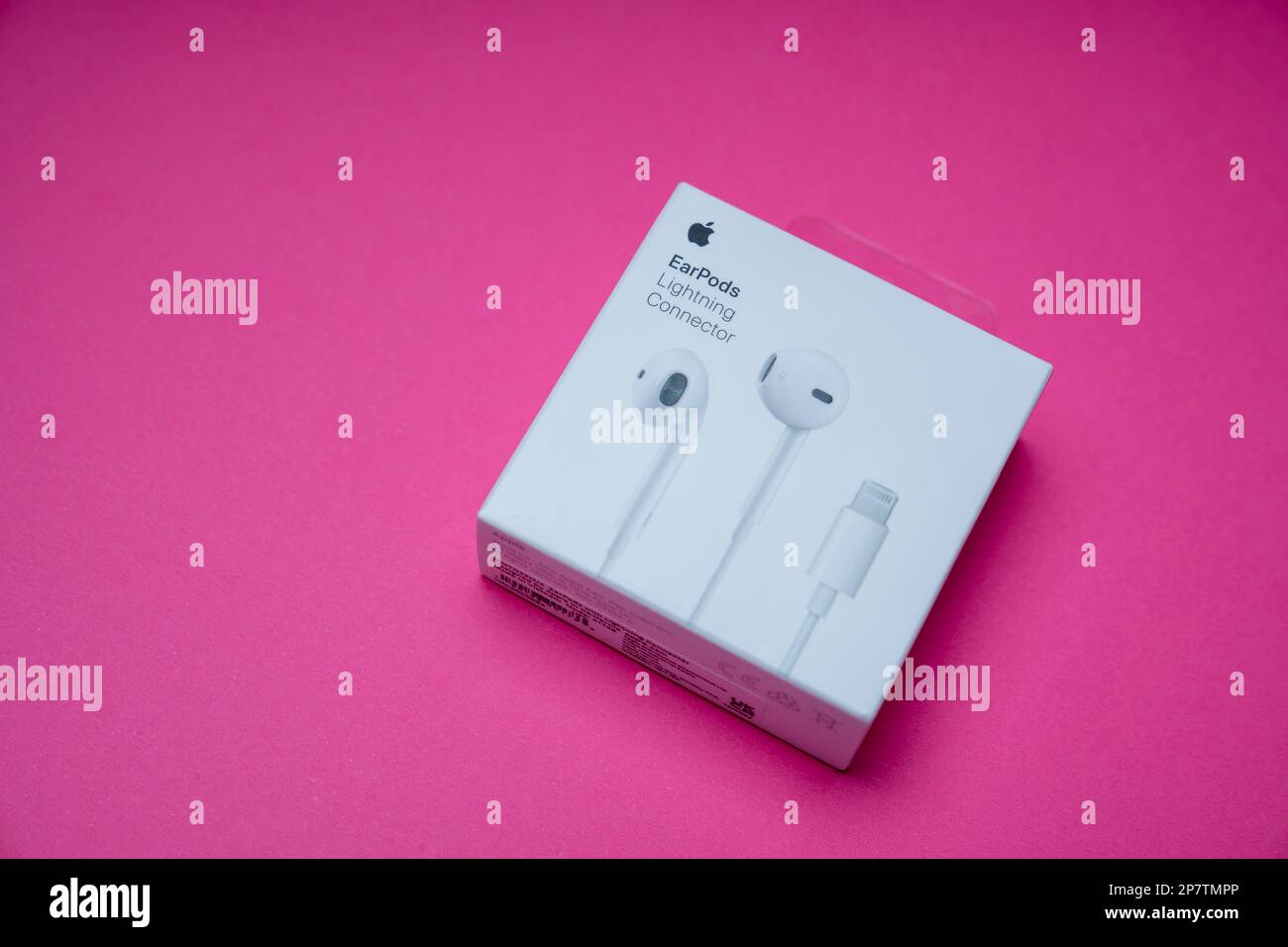 New Apple Earpods, Airpods white earphones for listening to music and podcasts in an closed box. Isolated pink background. Stock Photo