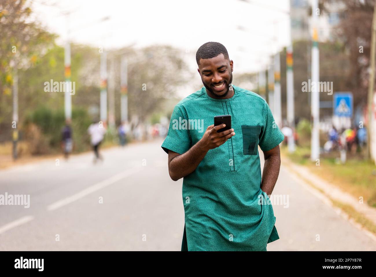 Confident young African man using smartphone outdoors, Tech-savvy individual exploring new apps on phone Stock Photo
